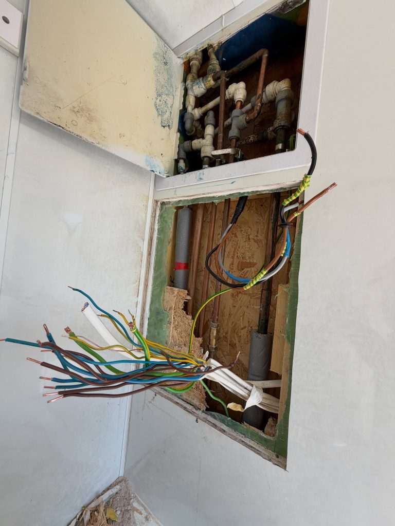 Stripped-out cabling and pipework exposed in a wall recess