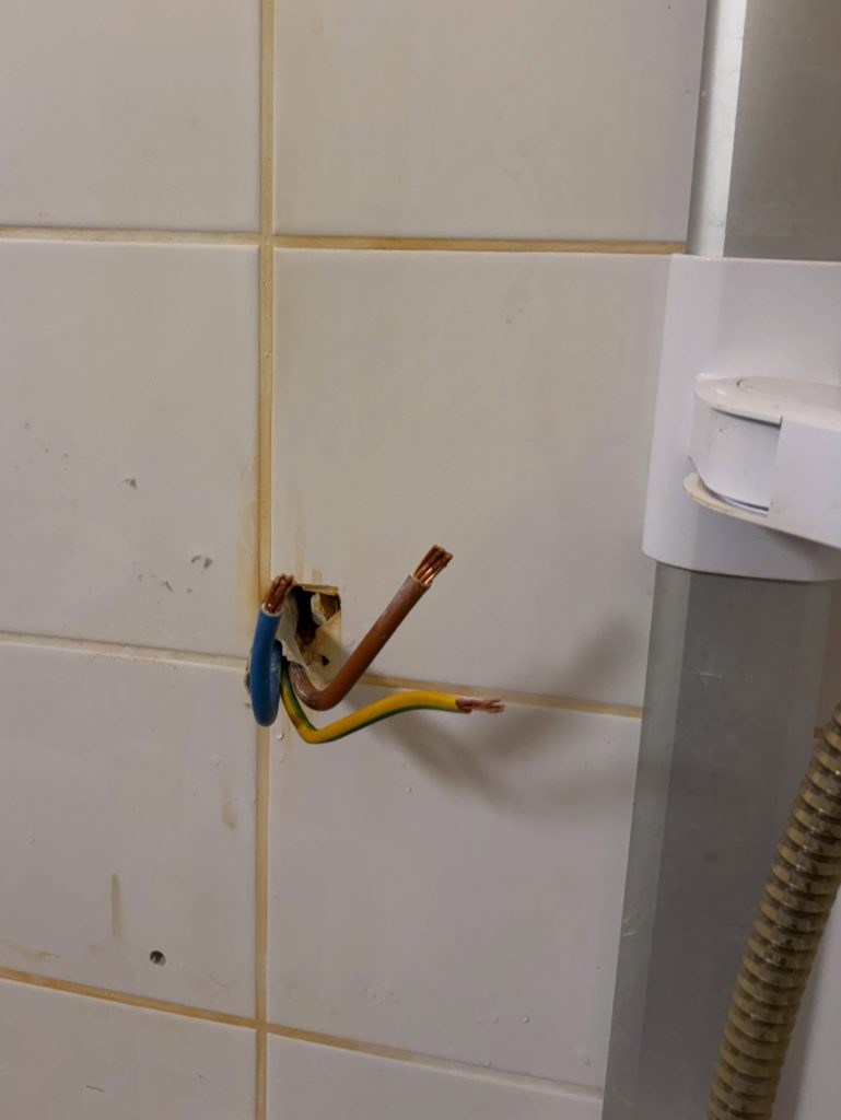 Bare shower supply cable tails left in a tiled bathroom wall